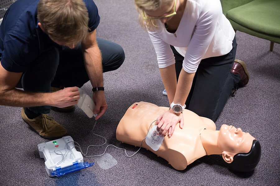 Two people using an AED device on a training dummy