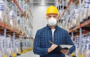 a warehouse worker wearing a respirator mask and hard hard holding a clipboard