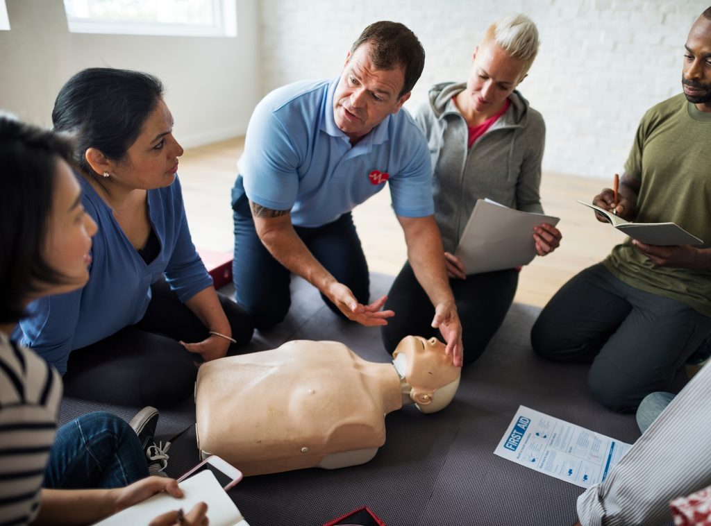 an instructor performing hands-on CPR and first aid training to a classroom of students